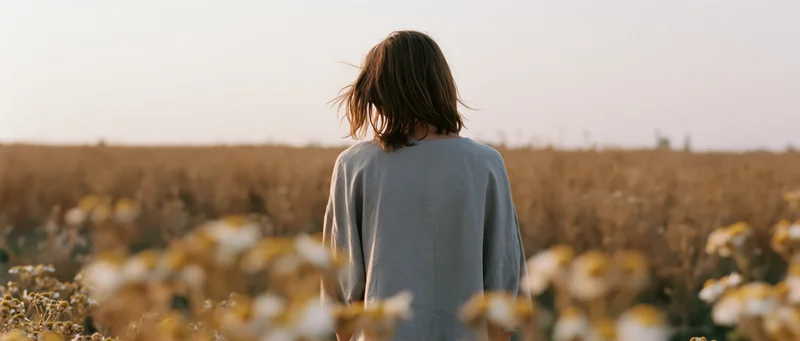 Woman standing with back to camera in a golden field of wildflowers at sunset