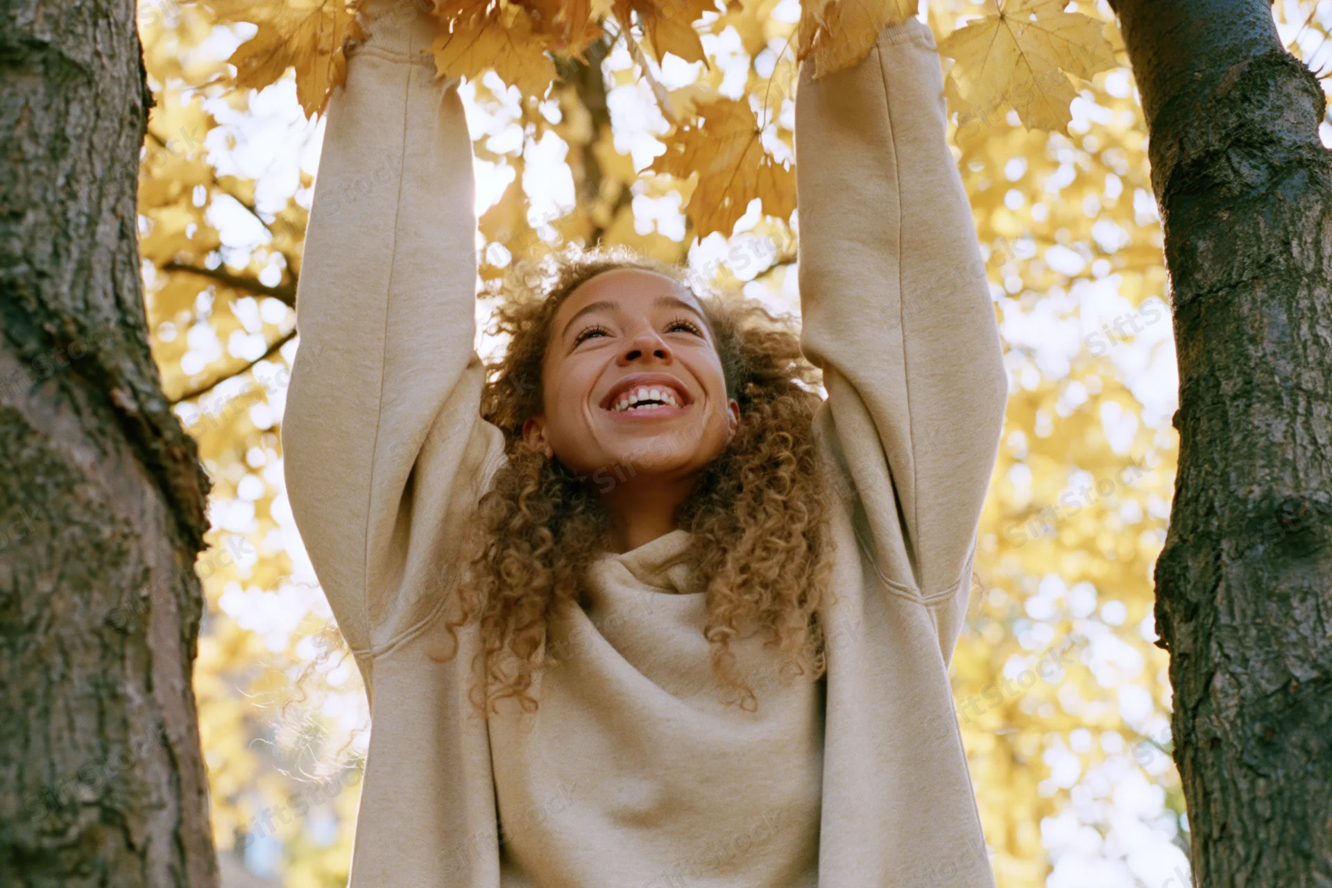 Young woman smiling with arms raised among autumn maple leaves in a park