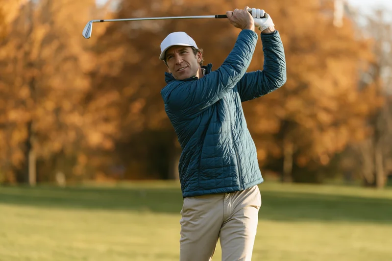 Man swinging golf club on a golf course in autumn