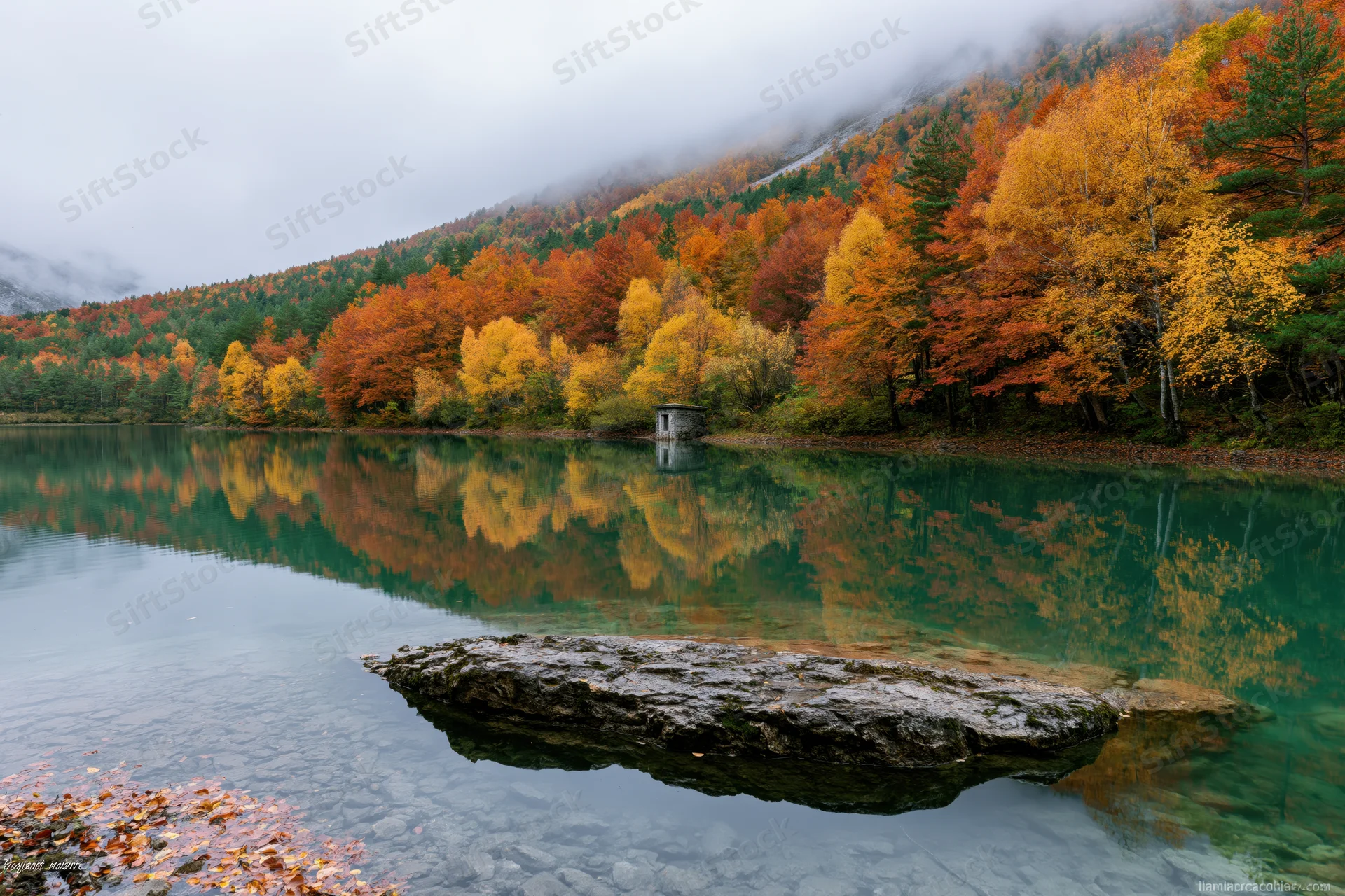 Calm mountain lake reflecting autumn forest and stone structure on misty shore