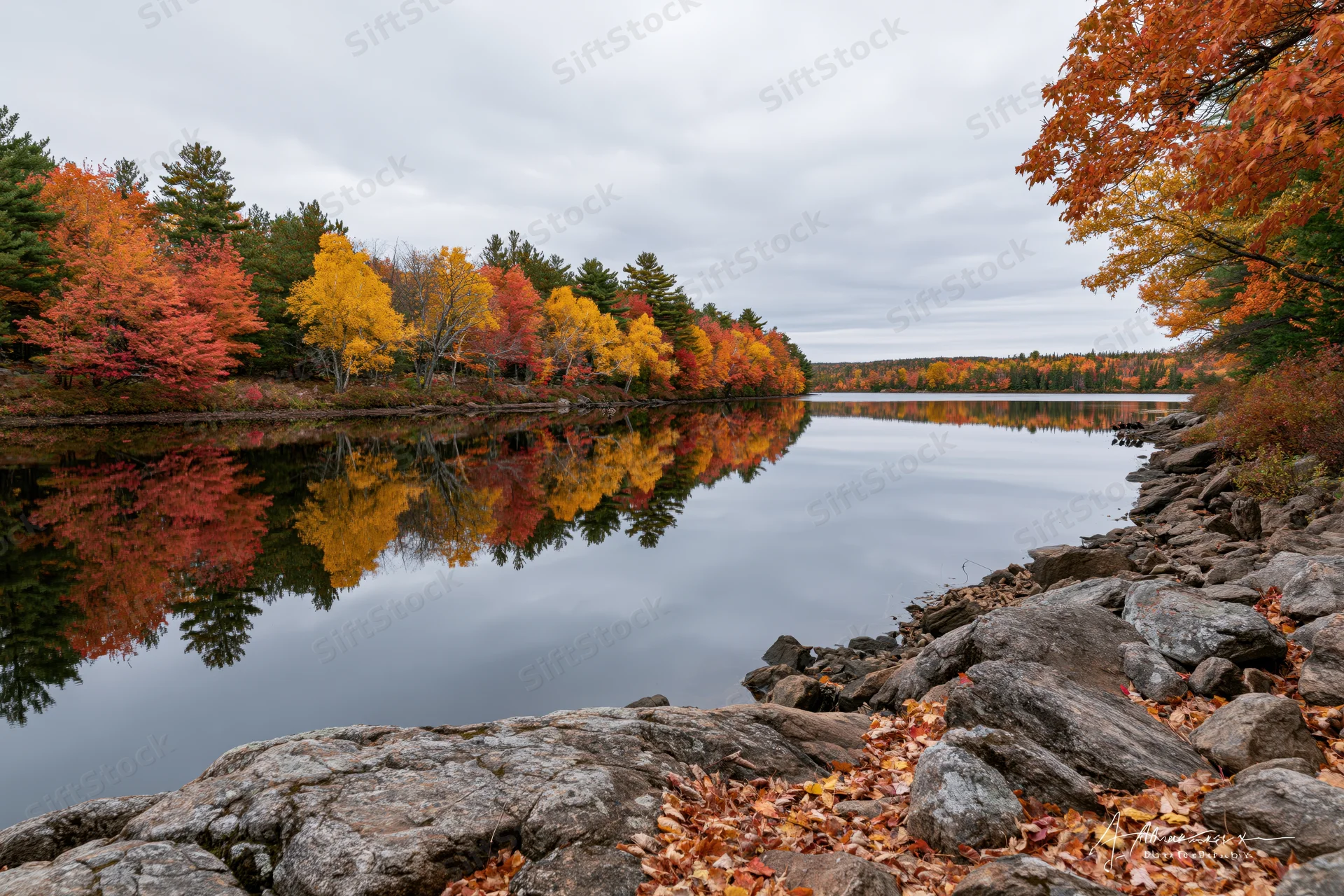 Calm lake reflecting autumn trees along rocky shore