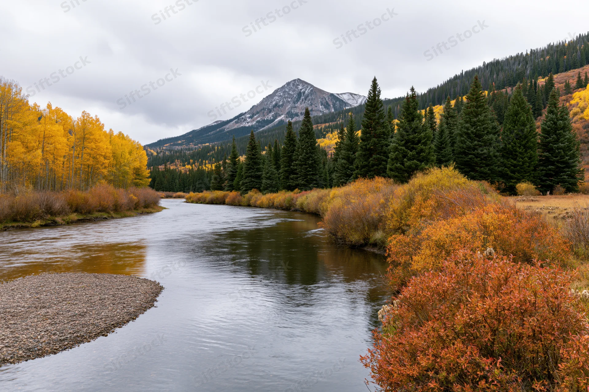 Calm river winding through mountain valley in autumn with colorful trees and snow-capped peak in background