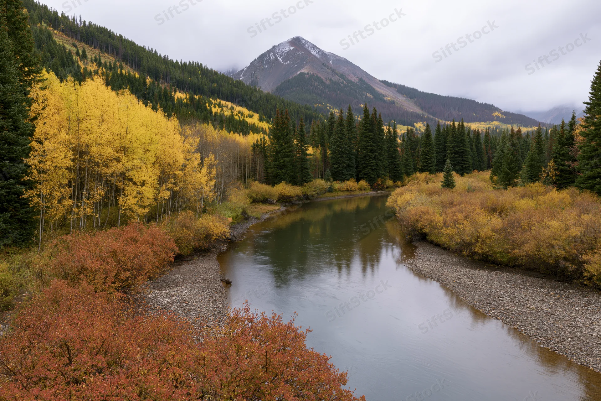 Calm river winding through a mountain valley in autumn with colorful trees and snow-capped peak in background