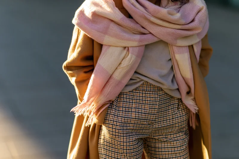 Woman wearing pink scarf and brown coat with checkered trousers on city sidewalk