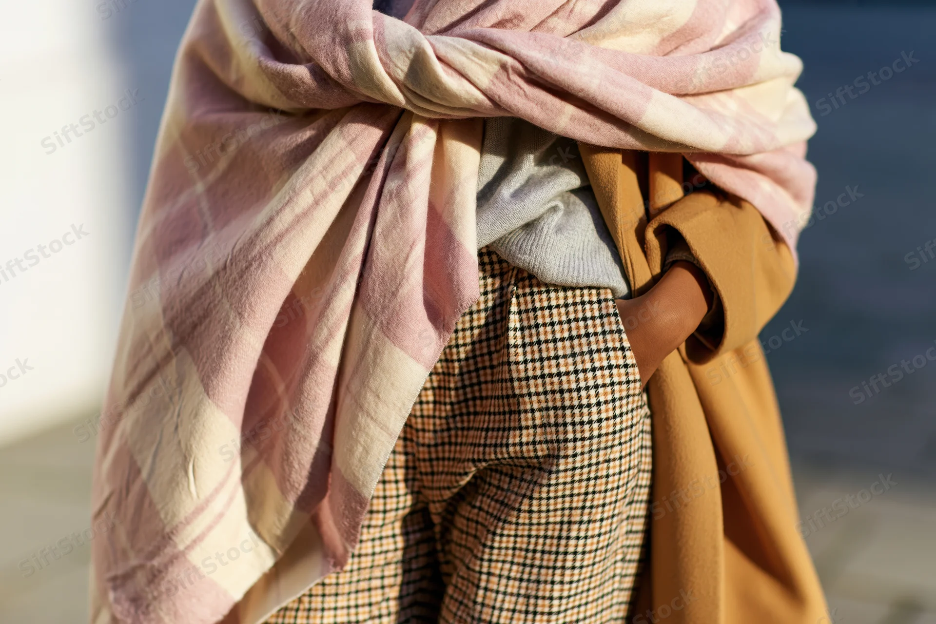 Woman wearing layered autumn outfit with pink plaid scarf and houndstooth skirt on city sidewalk