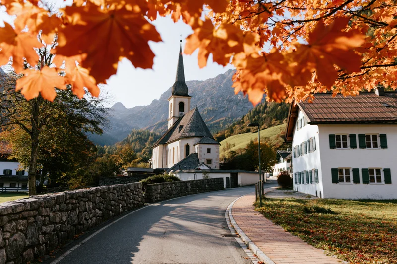 Autumn leaves framing a church and houses along a winding road in a small alpine village