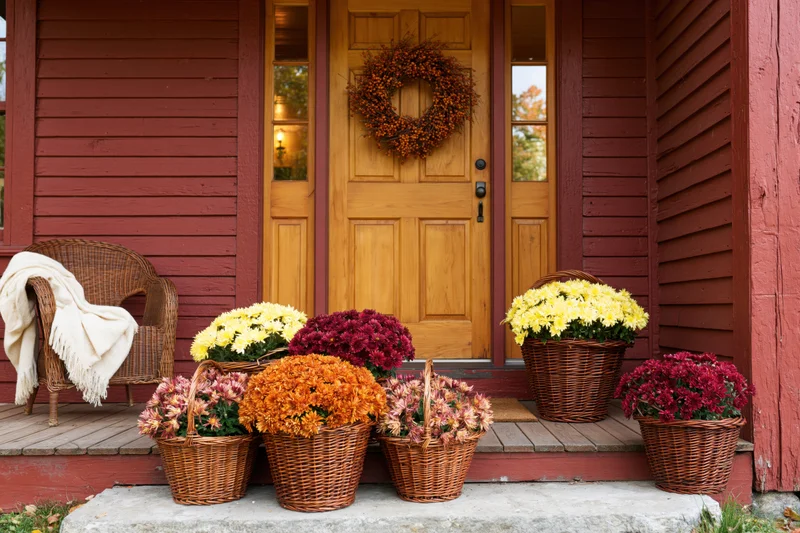 Autumn flowers in wicker baskets arranged on a red wooden porch with a wreath on the door