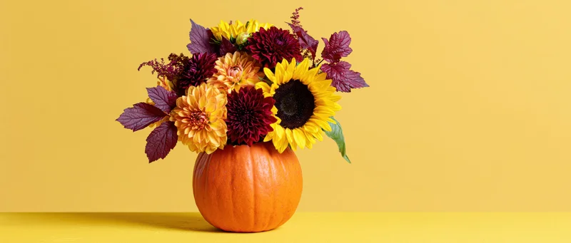 Hollowed orange pumpkin used as vase holding autumn flowers on yellow surface