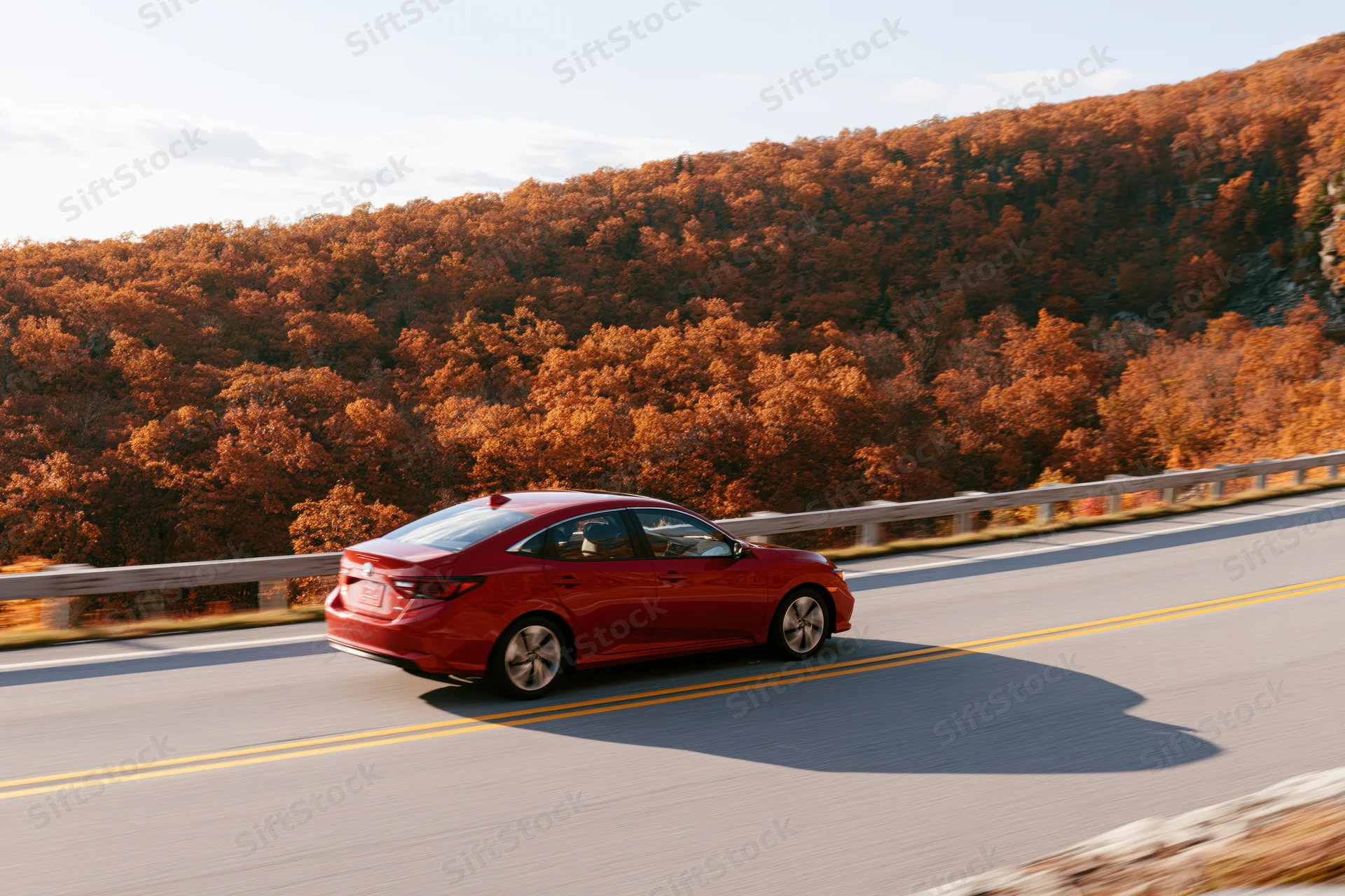 Red sedan driving on winding mountain road surrounded by autumn foliage