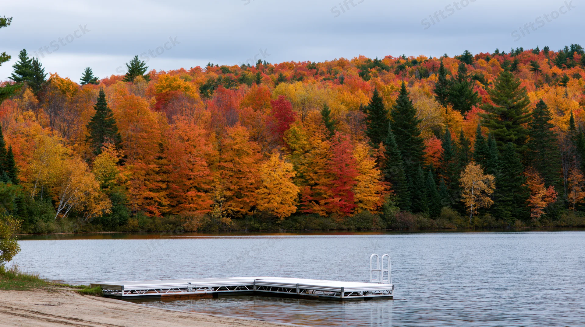 White metal dock extending into calm lake surrounded by autumn forest with colorful foliage