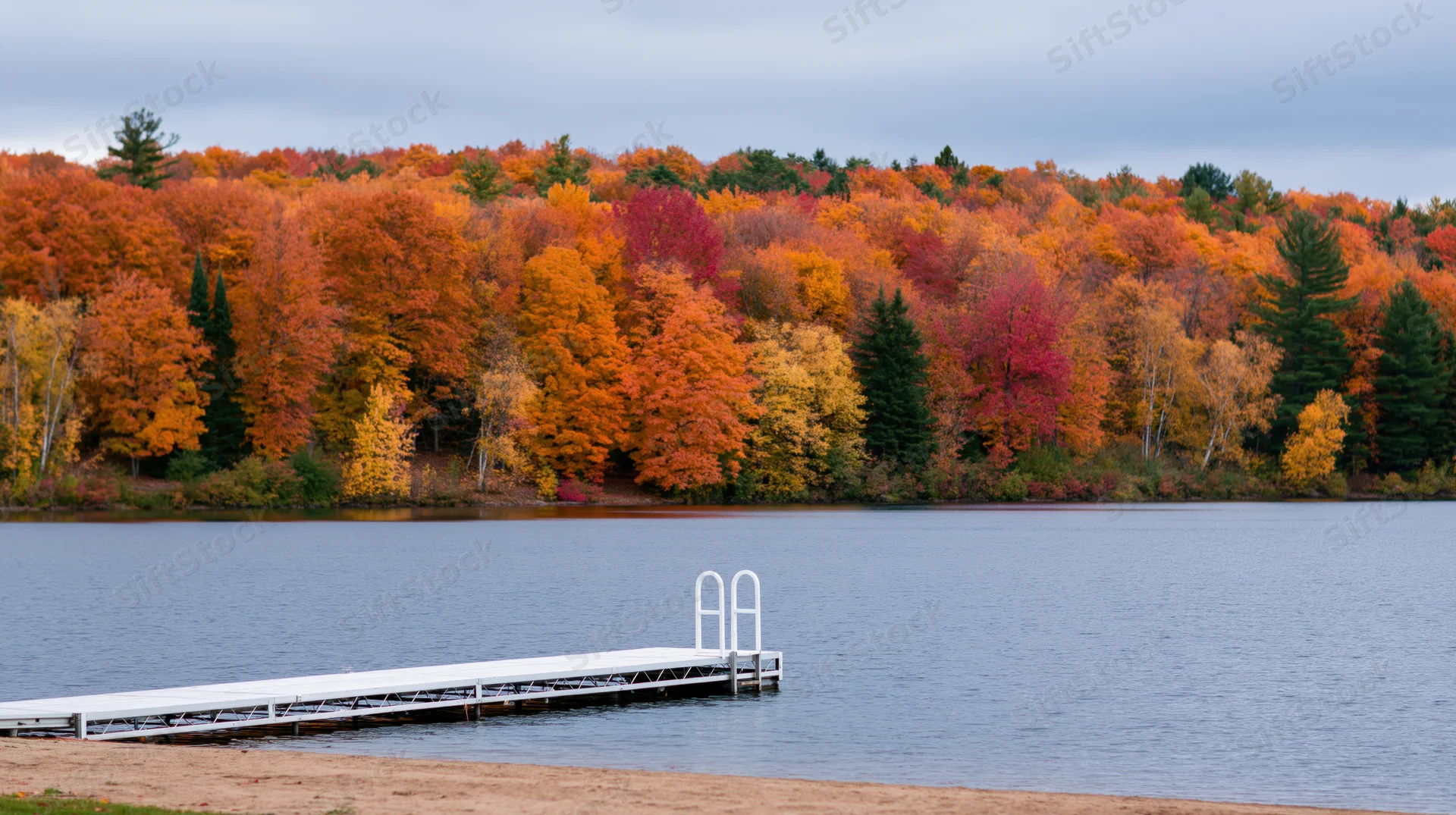 White metal dock extending into calm lake with autumn trees lining the shore