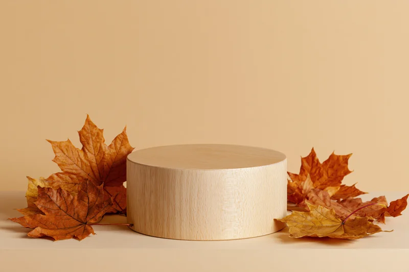 Wooden cylindrical podium on a flat surface surrounded by autumn maple leaves