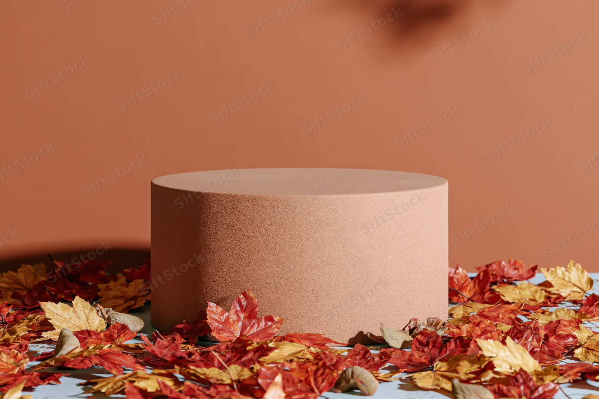 Round terracotta pedestal on a flat surface surrounded by autumn maple leaves