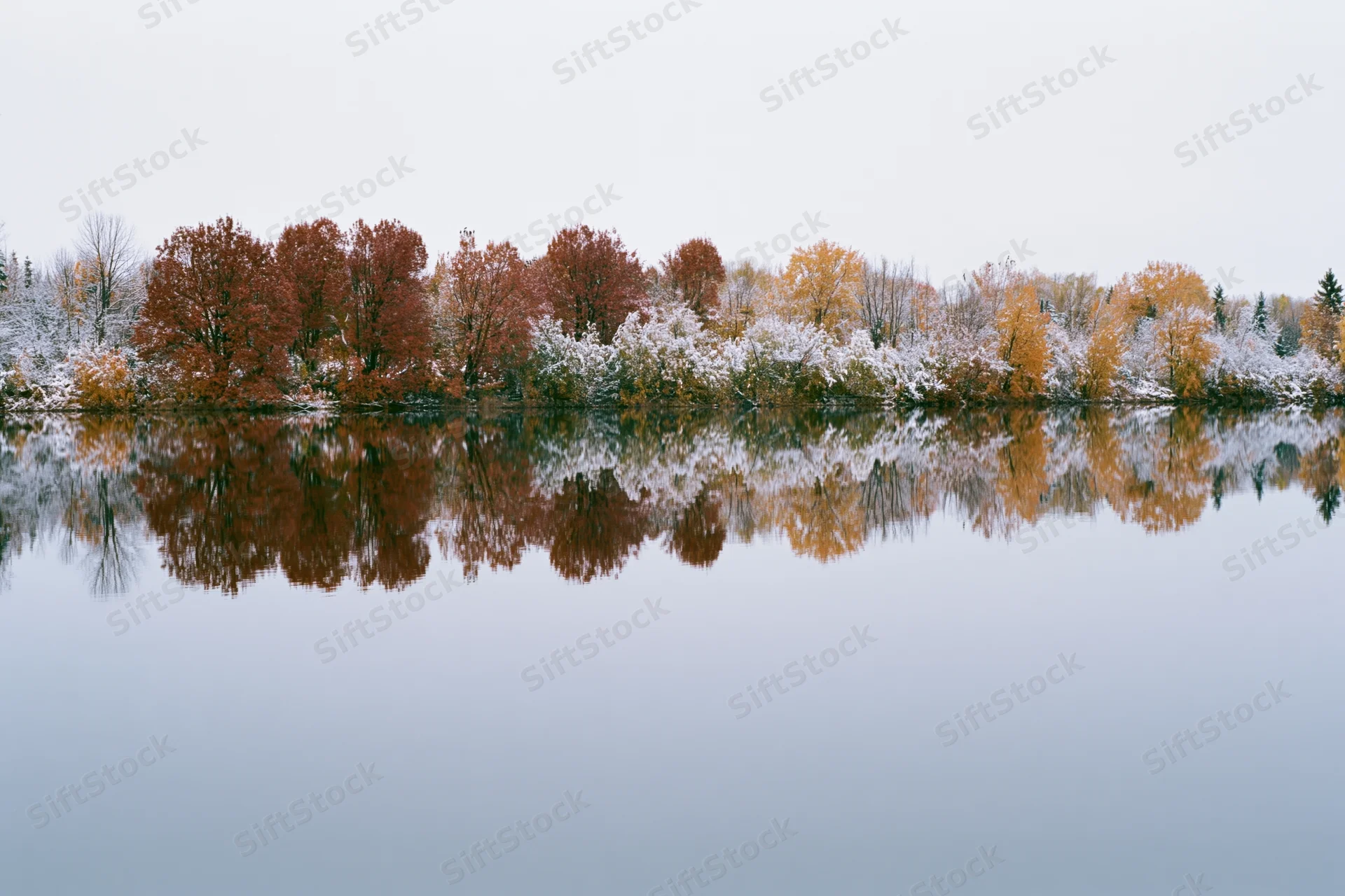 Still lake reflecting autumn trees along the shore under overcast sky