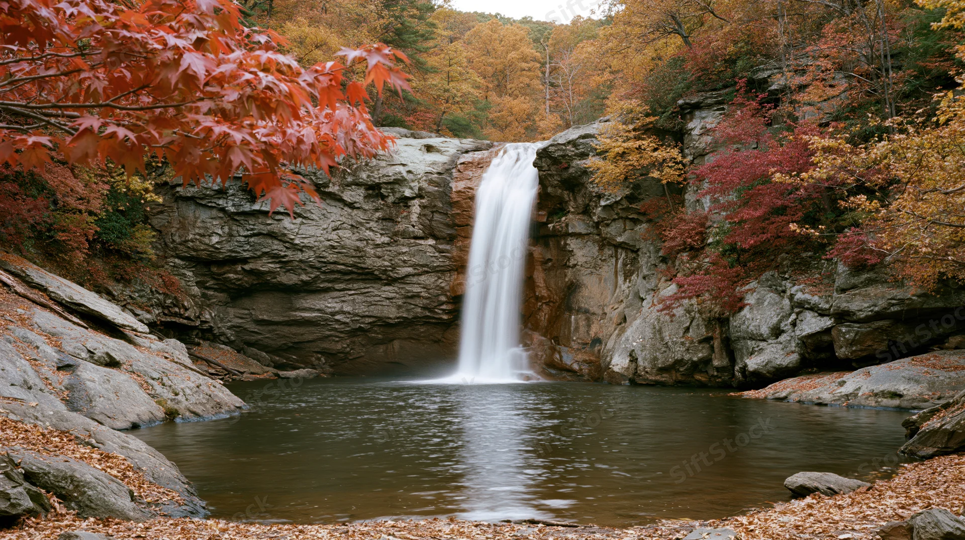 Waterfall cascading over rocky cliff into pool surrounded by autumn foliage