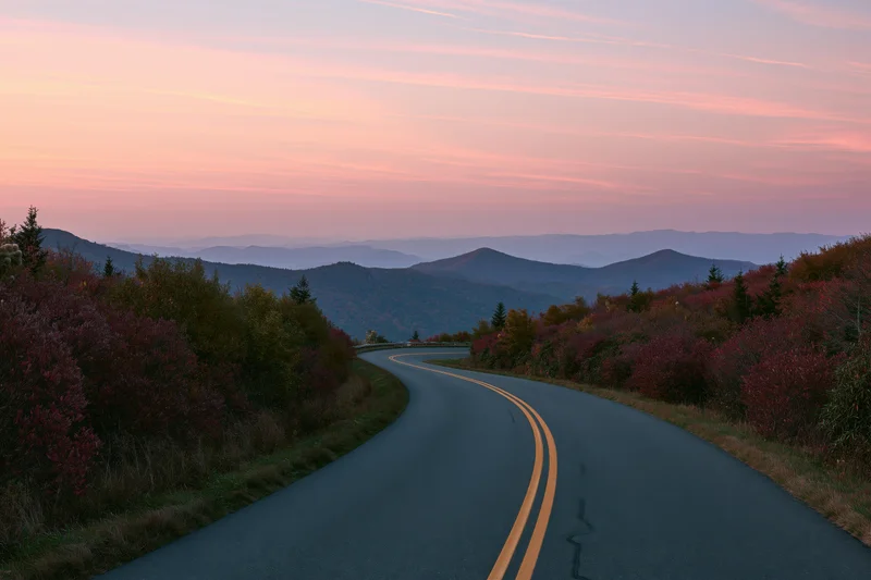 Winding asphalt road through mountain landscape at sunset with autumn foliage on both sides