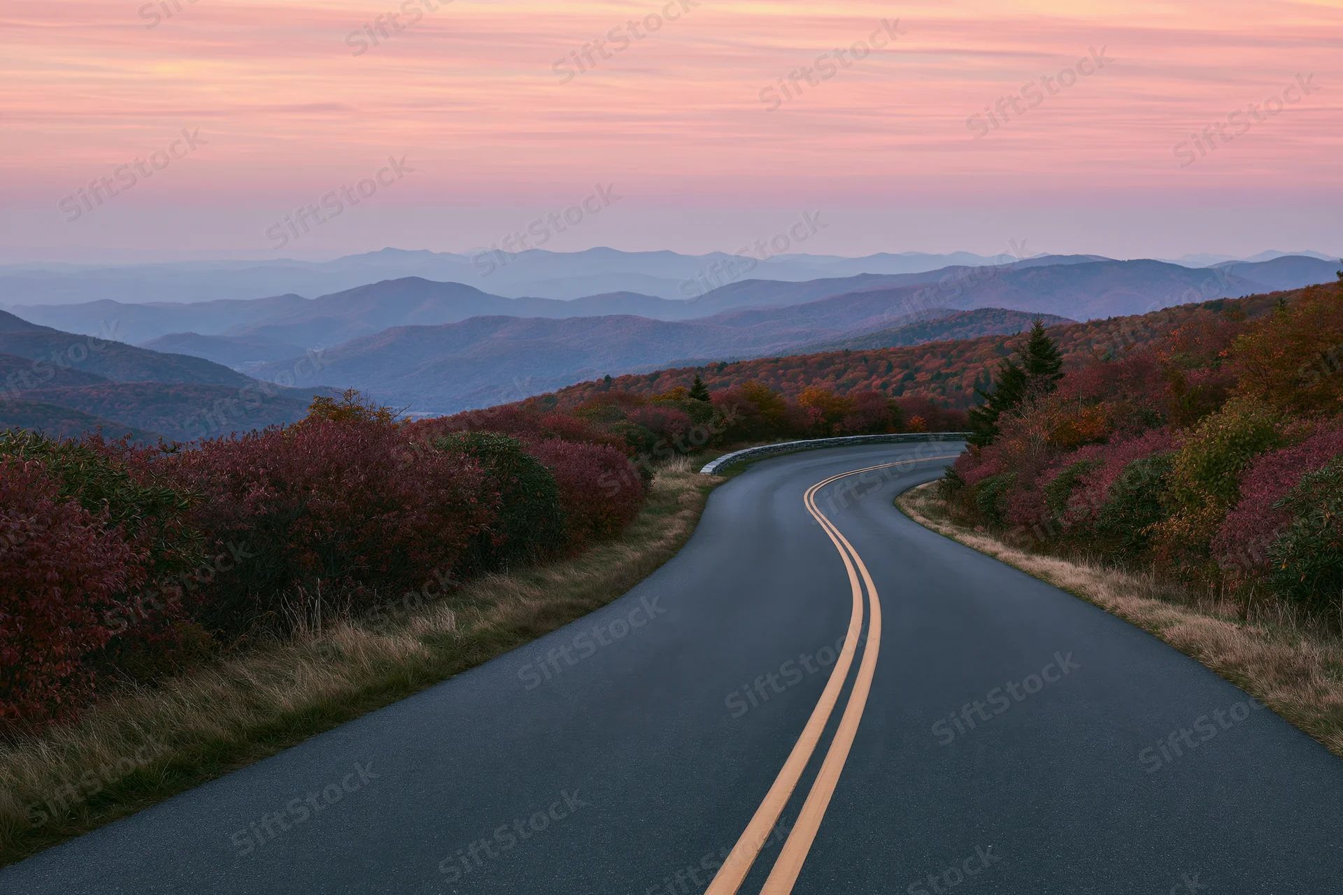 Winding asphalt road through autumn forested mountains at sunset