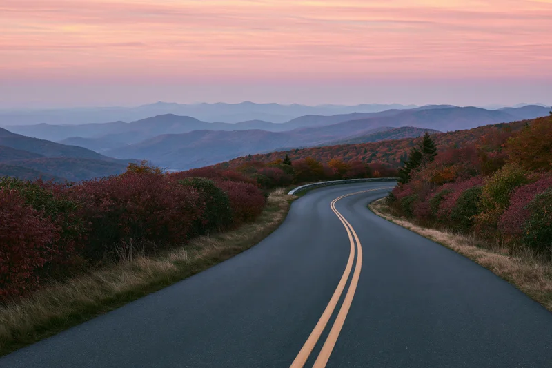 Winding asphalt road through autumn forested mountains at sunset