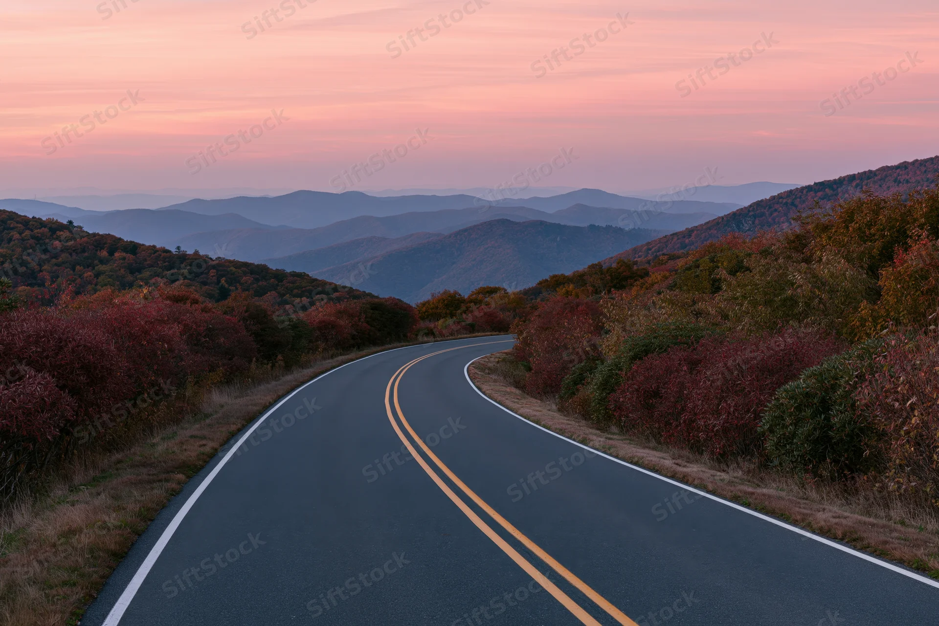 Winding two-lane highway through autumn forested mountains at sunset