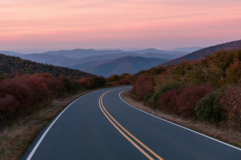 Winding two-lane highway through autumn forested mountains at sunset
