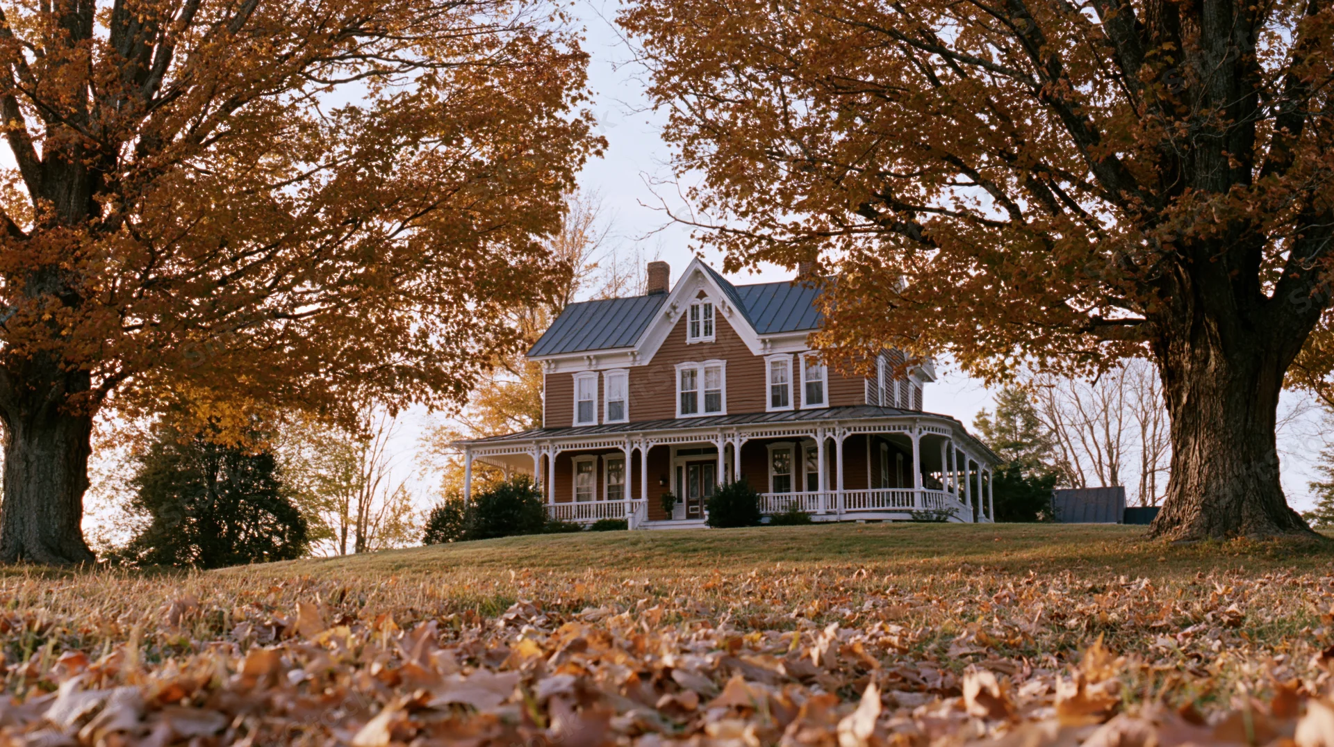 Victorian farmhouse with wraparound porch surrounded by autumn trees and fallen leaves on lawn