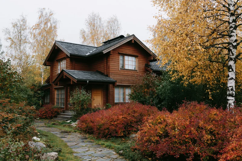 Two-story wooden country house surrounded by autumn foliage and a stone pathway leading to the front door