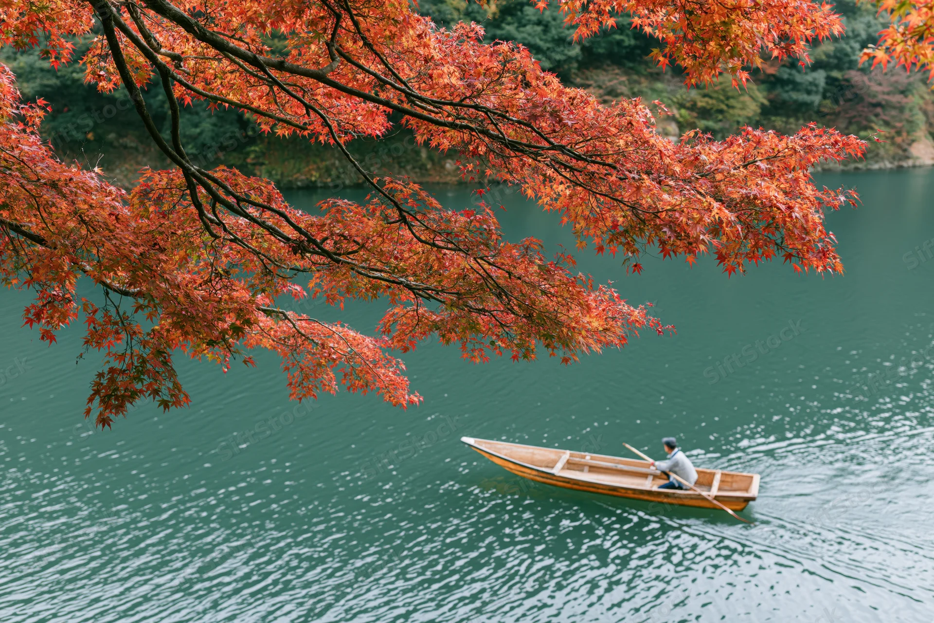 Man rowing a wooden flat-bottomed boat on a calm river beneath autumn maple trees
