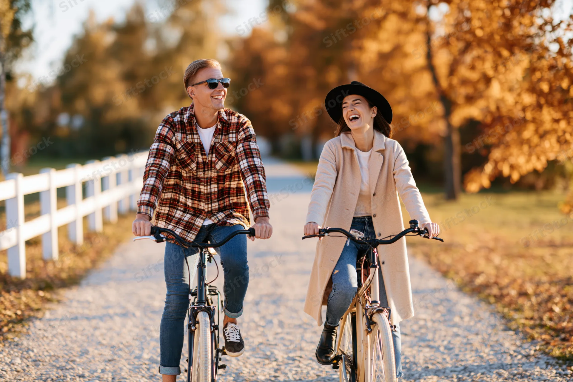 Young couple riding bicycles side by side on a gravel path in autumn park