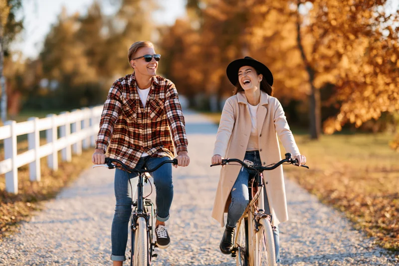 Young couple riding bicycles side by side on a gravel path in autumn park