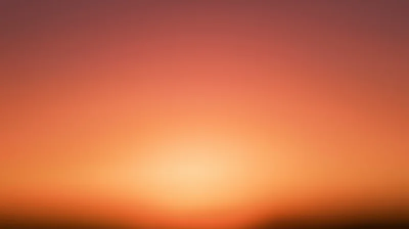 Smooth gradient of orange and pink hues across a blurred sky at dusk
