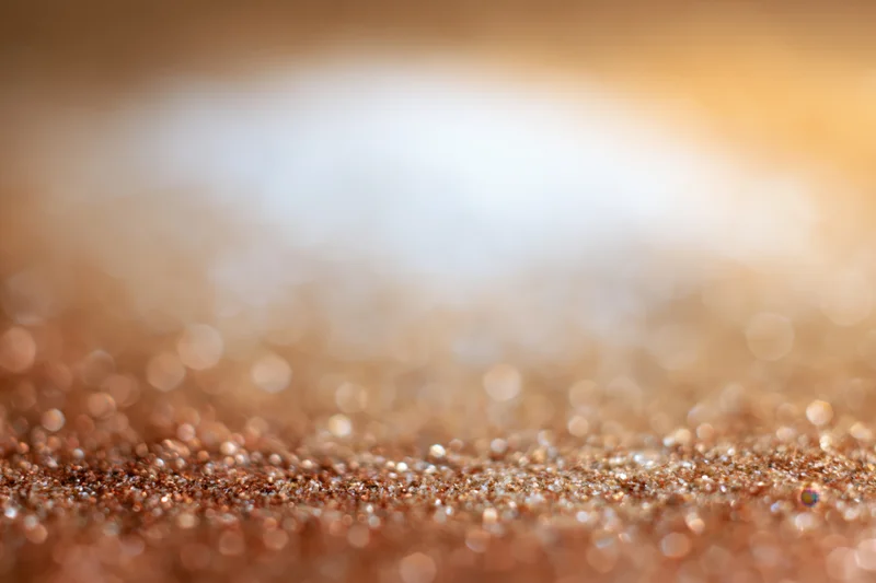 Golden glitter particles scattered across a soft defocused background with warm bokeh light