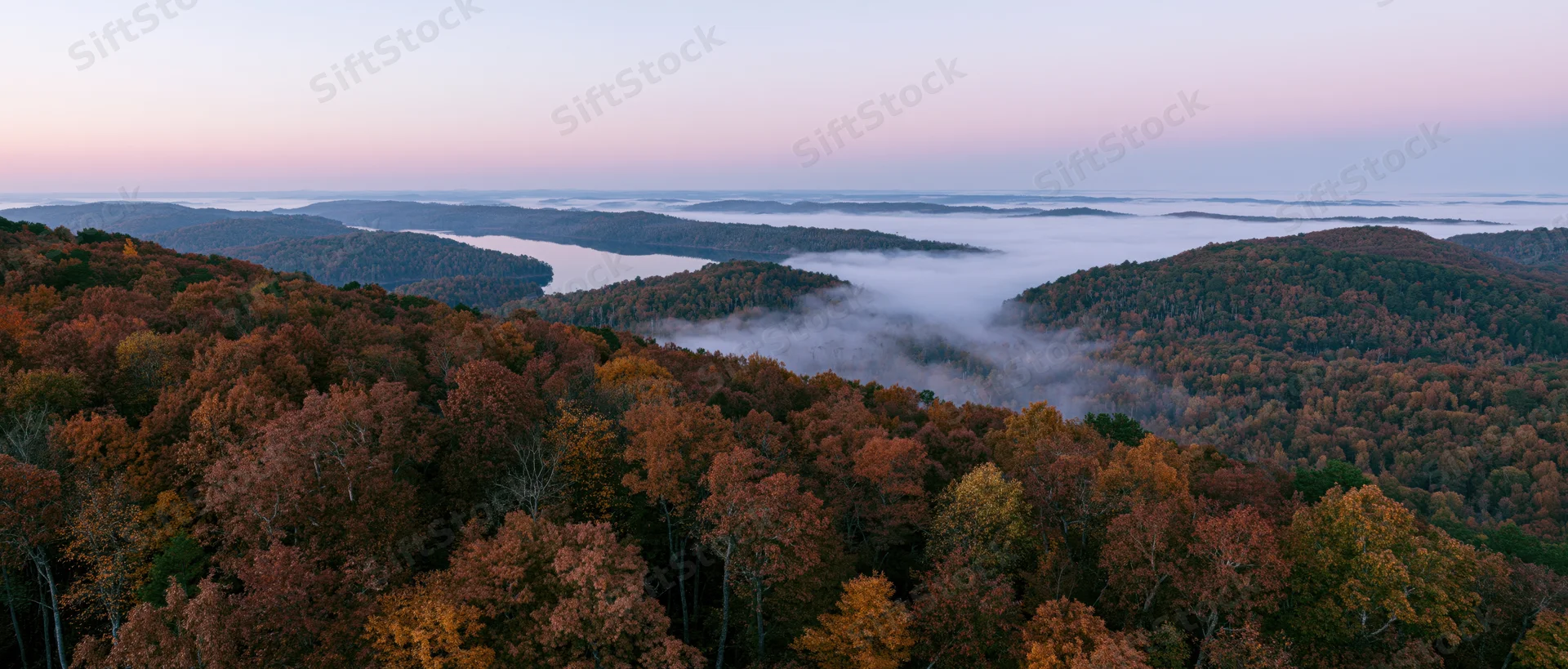 Aerial view of autumn forest canopy with misty valley and river below at dawn