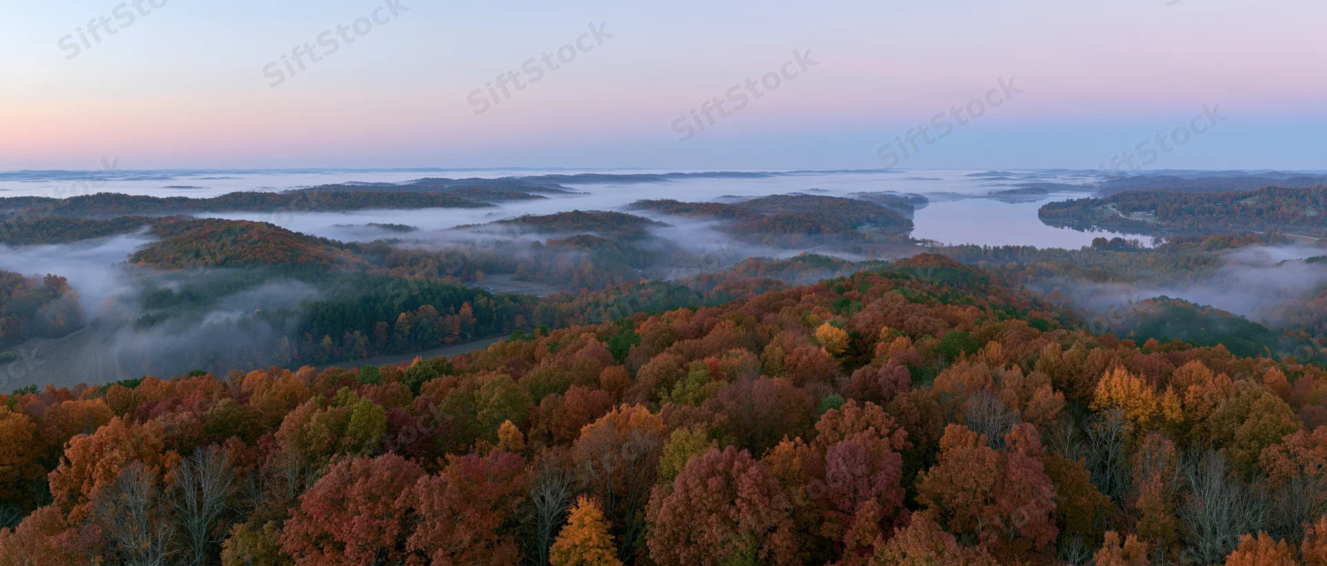 Aerial view of autumn forest canopy with misty valleys and colorful foliage at dawn