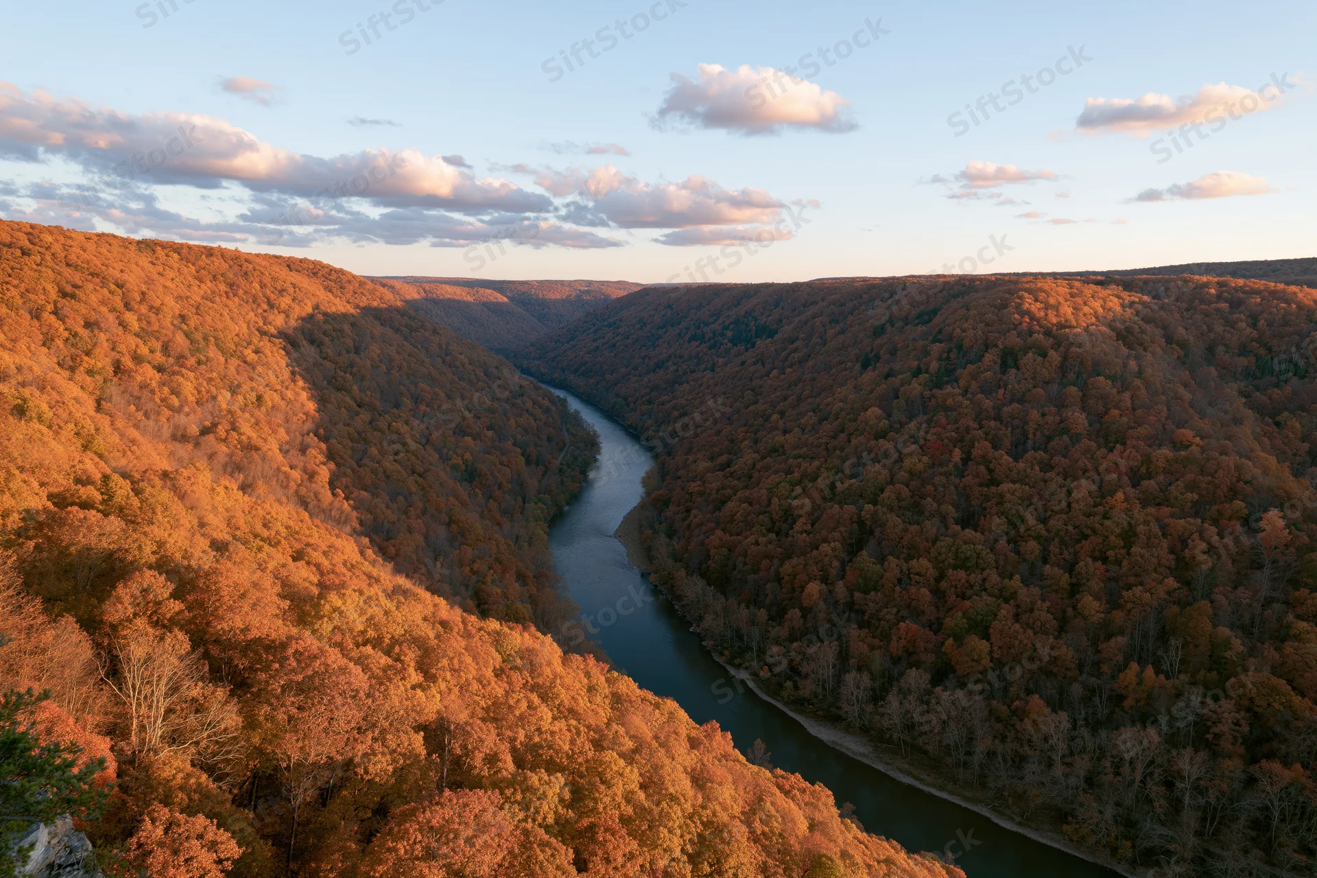 Aerial view of a river winding through a dense autumn forest valley