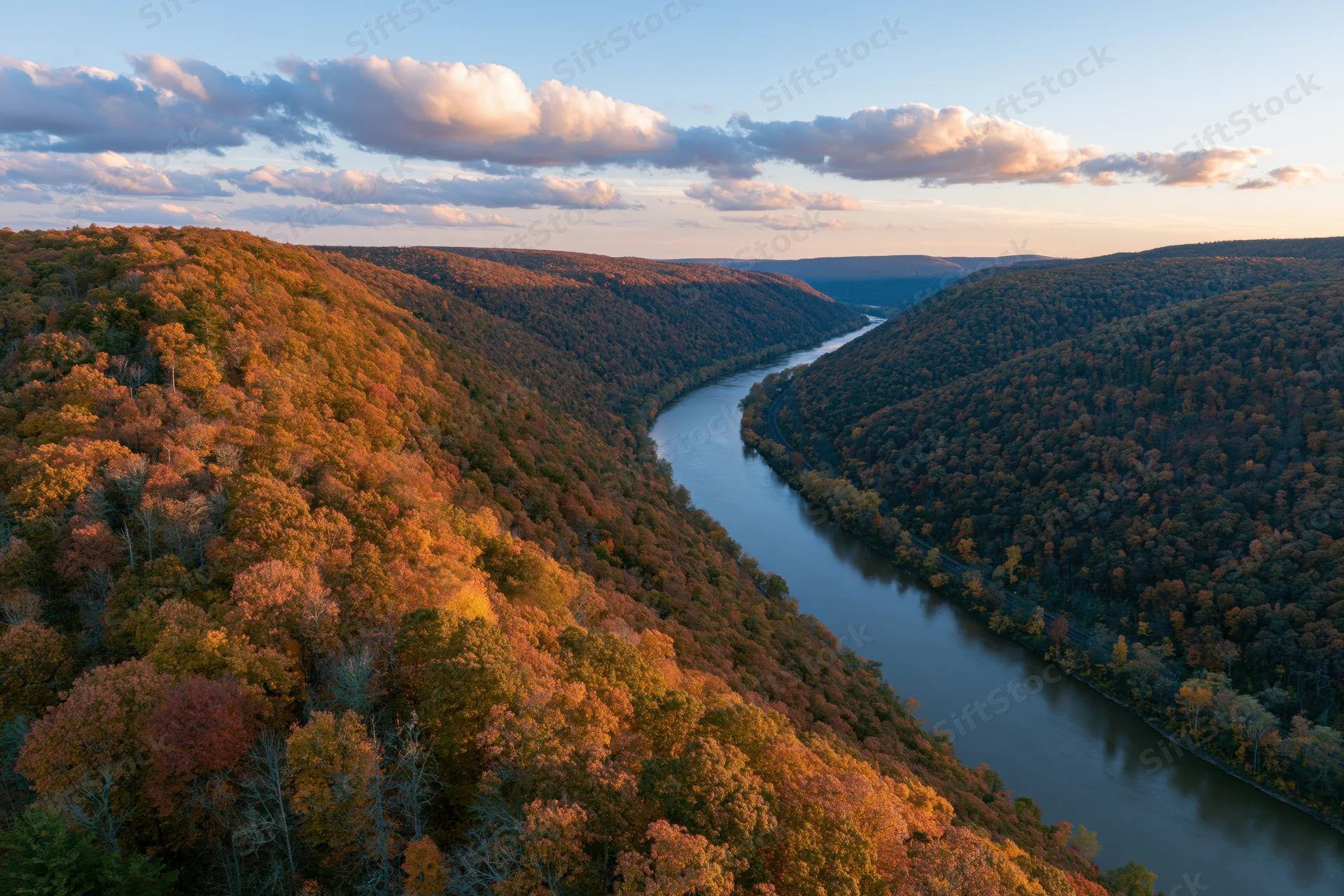 Aerial view of a winding river through a dense autumn forest valley