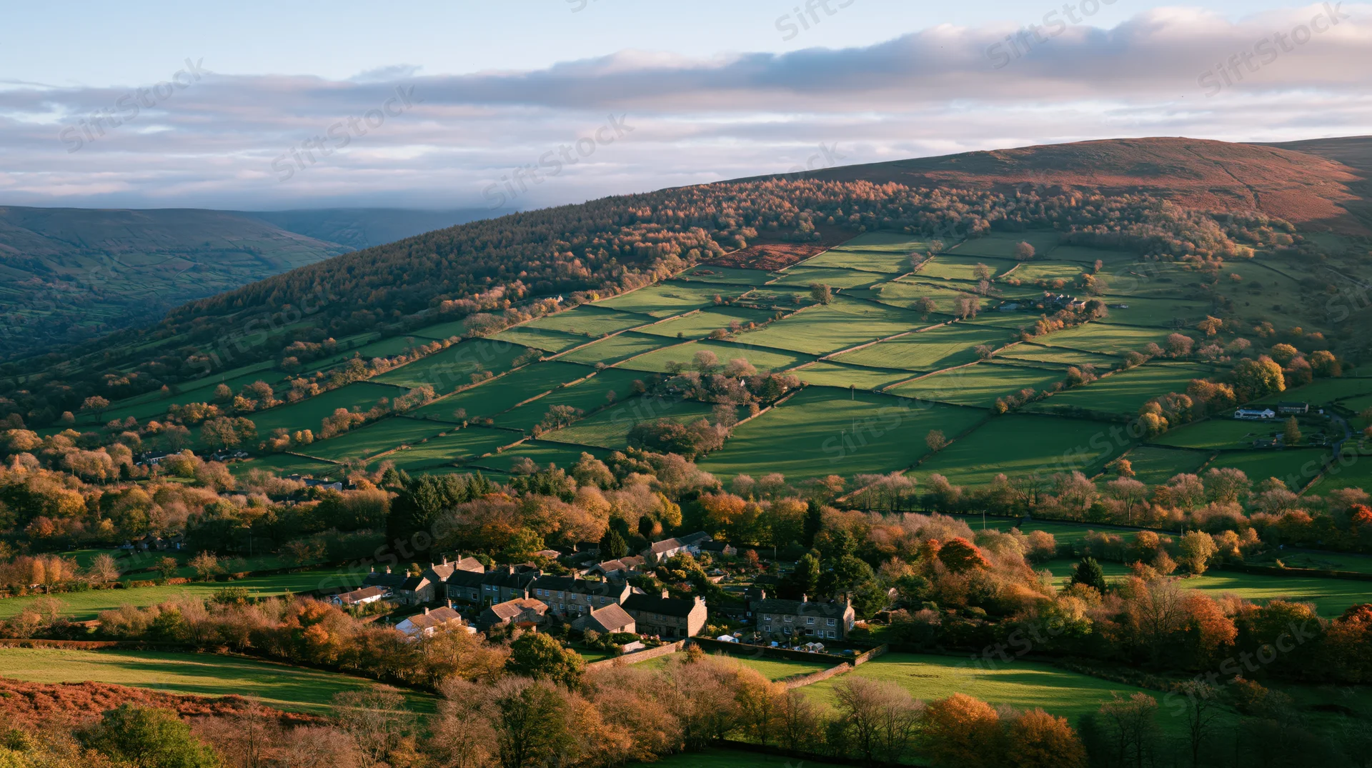 Aerial view of an english countryside valley in autumn with rolling green fields, hedgerows, and a small village nestled among autumnal trees
