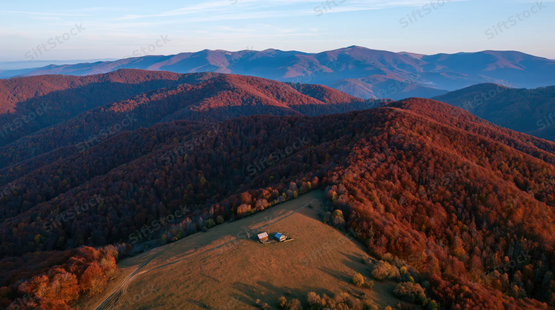 Aerial view of rolling carpathian hills covered in autumn forest with a small cabin on a meadow