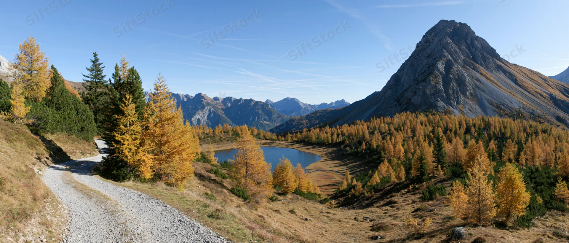 Winding gravel path through alpine autumn landscape with golden larch trees and mountain lake