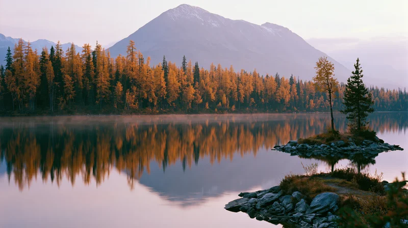 Alpine lake reflecting golden autumn trees at dawn with still water and distant mountain