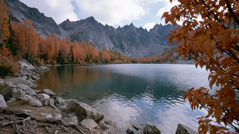 Alpine lake surrounded by jagged rocky peaks in autumn with orange foliage and calm water reflecting the sky
