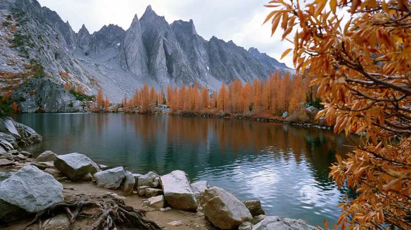 Alpine lake reflecting jagged rocky peaks surrounded by autumn-colored trees and boulders along the shore