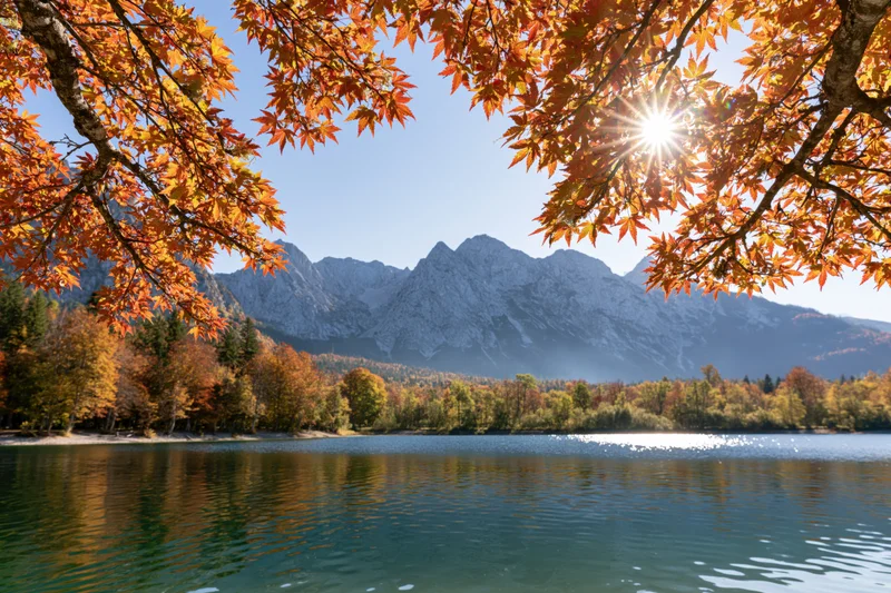 Alpine lake reflecting autumn trees and mountains under bright sun