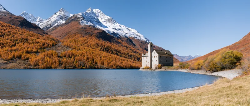 Alpine lake shoreline with church and snow-capped mountains in autumn landscape