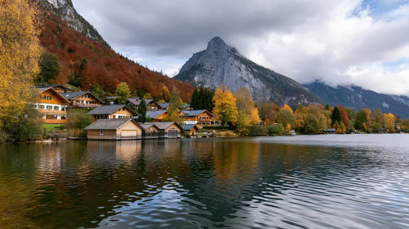 Alpine lakeside village with traditional guesthouses nestled among autumn trees and mountains reflected in calm water