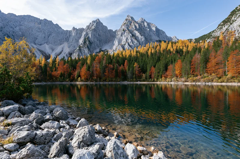Alpine lake reflecting autumn forest and jagged limestone peaks under a blue sky