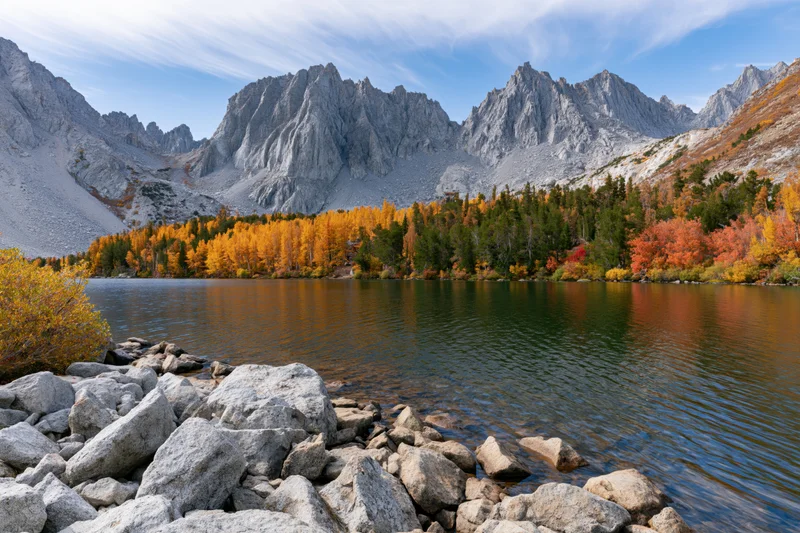 Alpine lake surrounded by jagged limestone peaks and autumn-colored trees under a clear blue sky