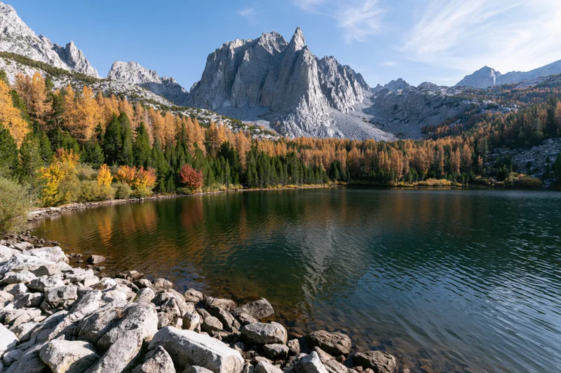 Alpine lake surrounded by jagged limestone peaks and autumn-colored trees under a clear blue sky