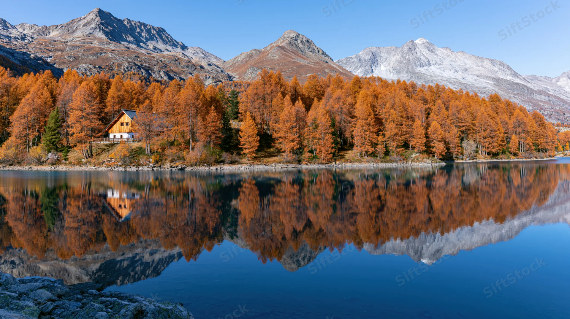 Calm alpine lake reflecting autumn trees and mountains in still water