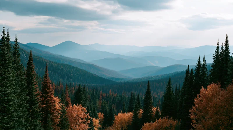Layered alpine ridgelines receding into misty distance through autumn forest valley