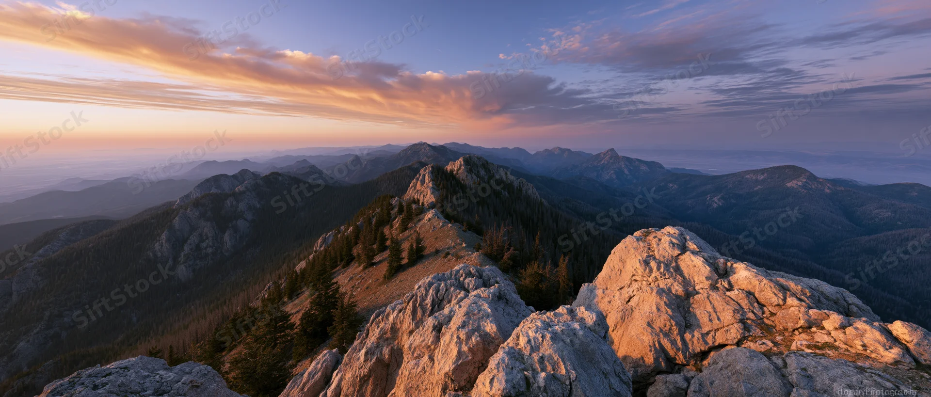 Alpine mountain panorama from rocky summit at sunset with forested valleys and layered peaks under twilight sky
